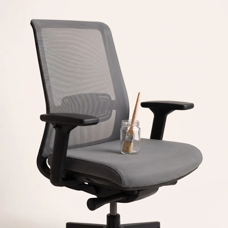 An empty office chair, a paintbrush in a glass jar on the seat
